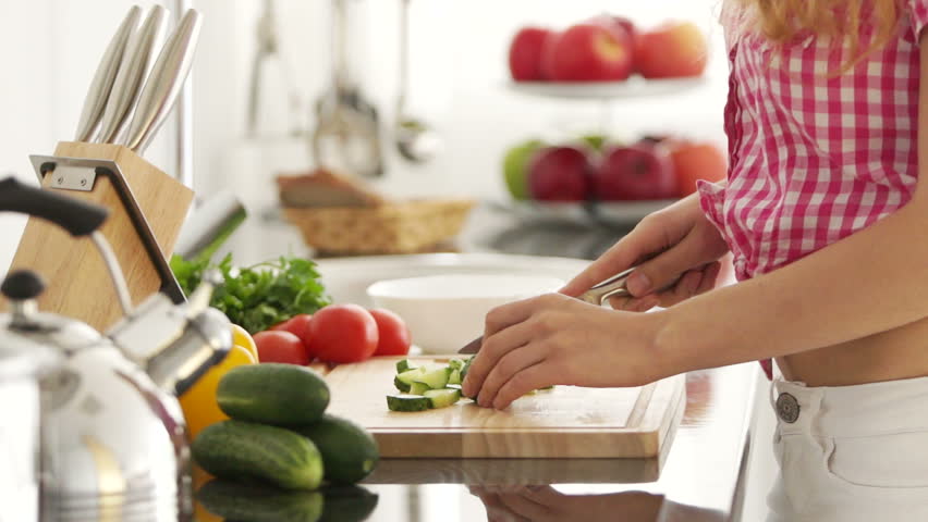 Young woman in kitchen cutting vegetables on cutting board
