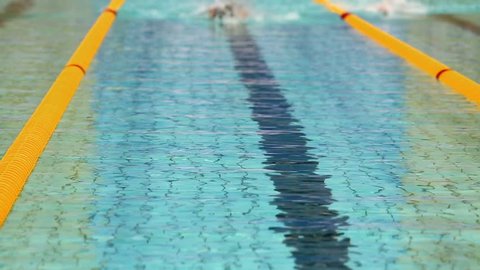 Three sportsmen swim in crawl style by tracks in swimming pool