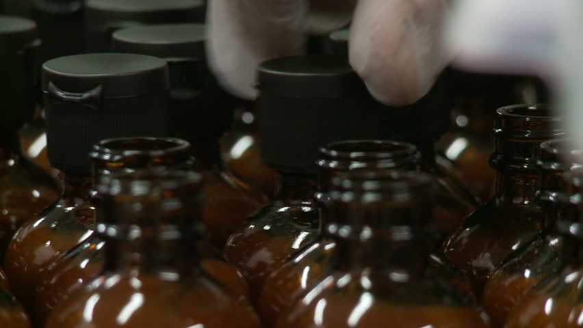 Short dolly shots across lines of sauce bottles having caps put on them.  Two
