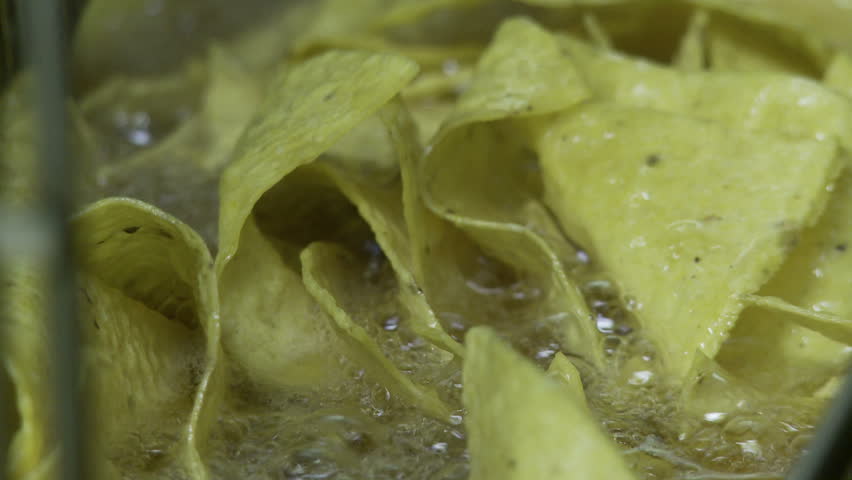 Close up of corn chips frying in a restaurant frier.  Hand held camera.