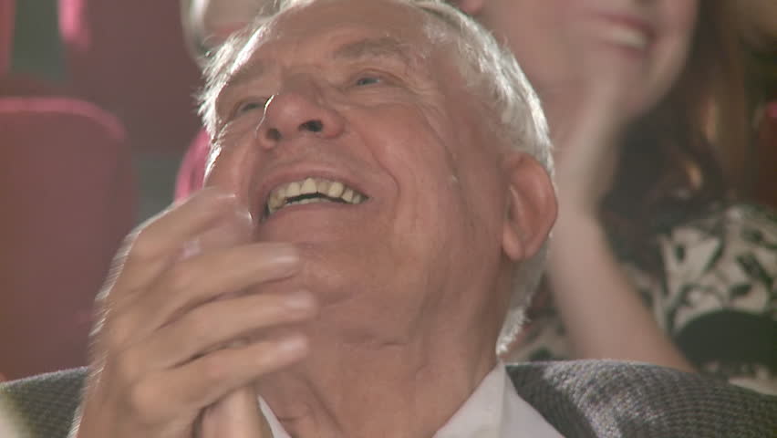 Close up on elderly man in a group of people sitting in theater, applauding