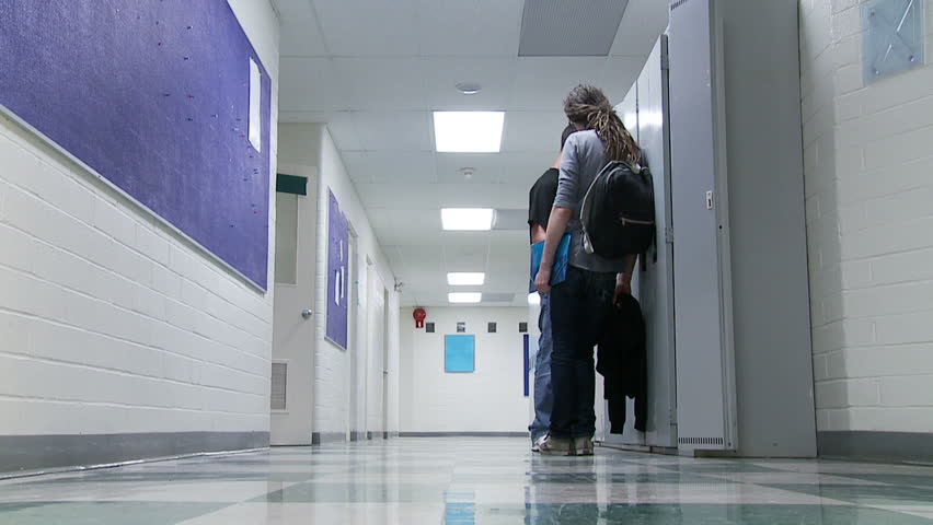 Group of girls walk past two boys hanging out in a high school corridor.  Speed