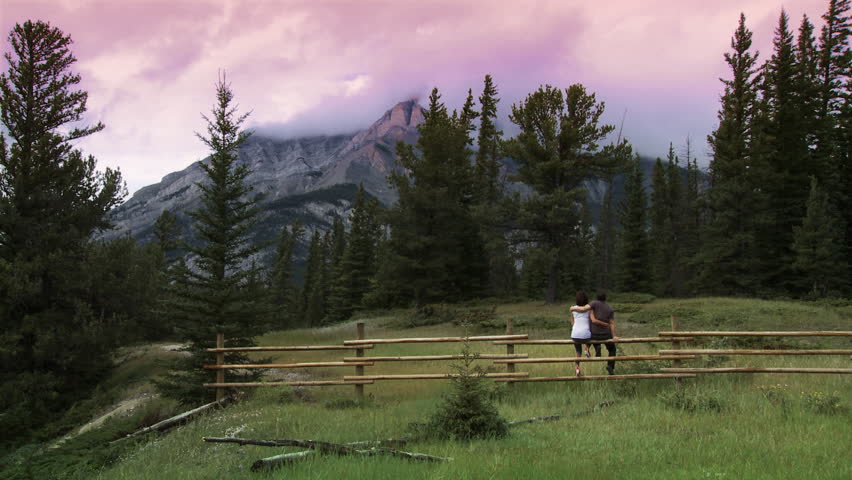 Wide shot of a loving young couple sit on a fence to look at the scenery of the