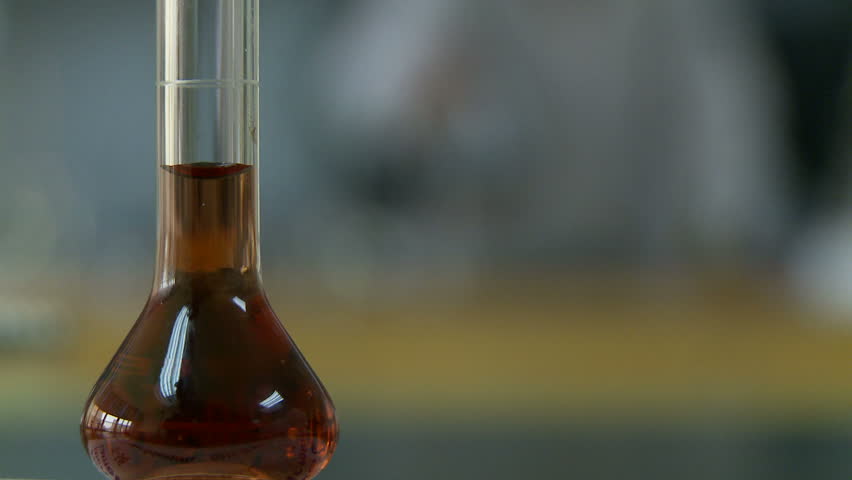 Flask of amber liquid in focus with soft focus laboratory background.  Loopable