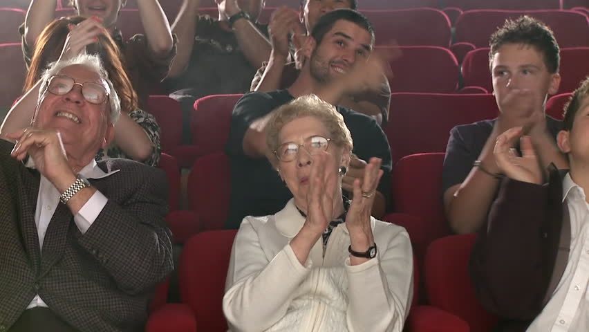 Group of people sitting in theater, applauding enthusiastically.  Slow motion,