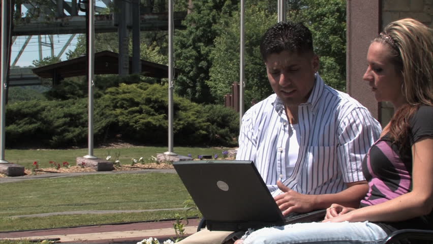A young couple uses a wireless laptop outside in the park.