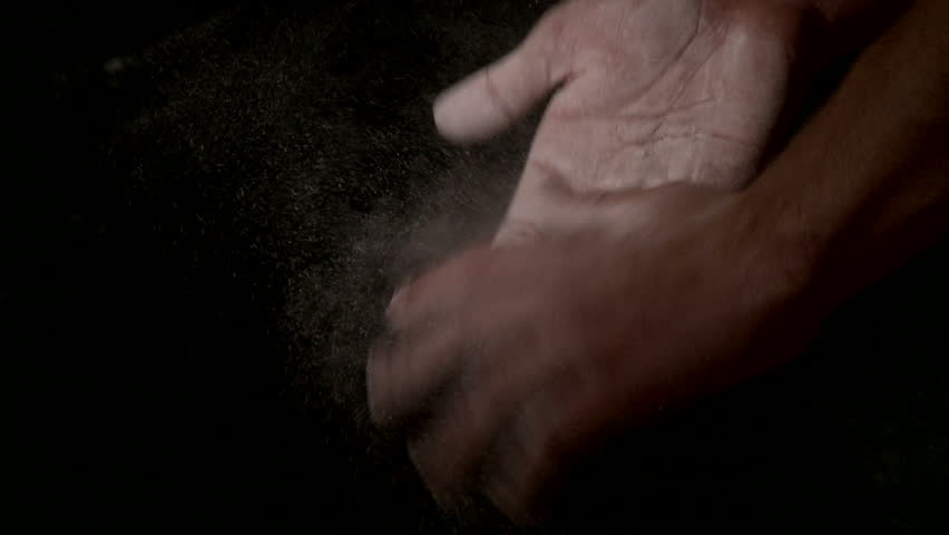 Two hands covered in chalk slap against each other, knocking white dust