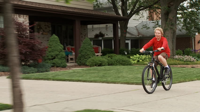 Smiling, happy young cyclist riding his bike on a sidewalk in a middle-class,