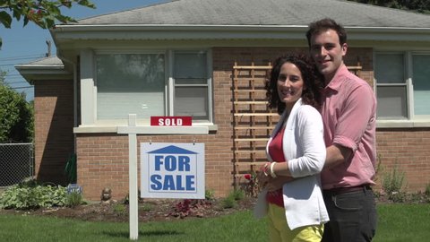 Happy young couple standing outside a sold house.