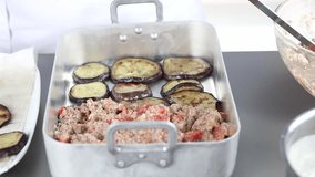 Moussaka being made: eggplant slices and minced meat being layered in a baking dish