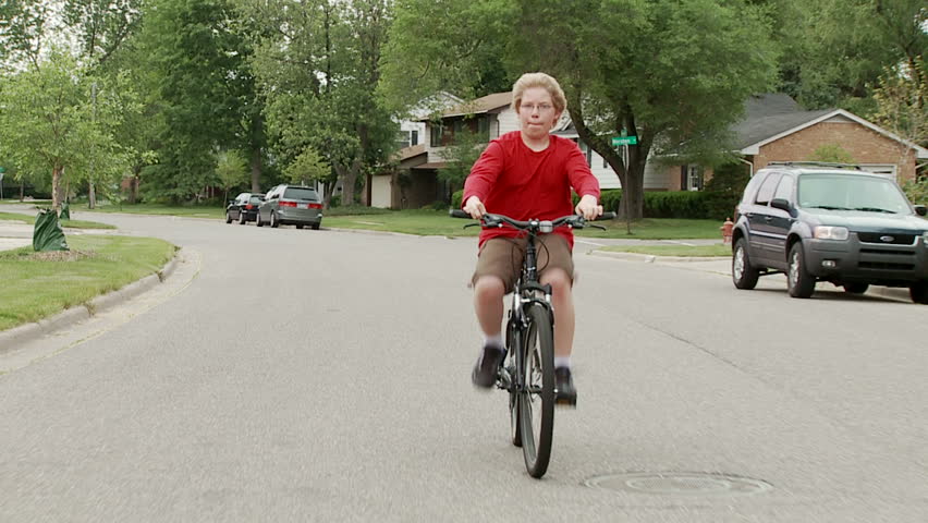 Boy rides bicycle in the road through middle-class, mid-western American suburb.