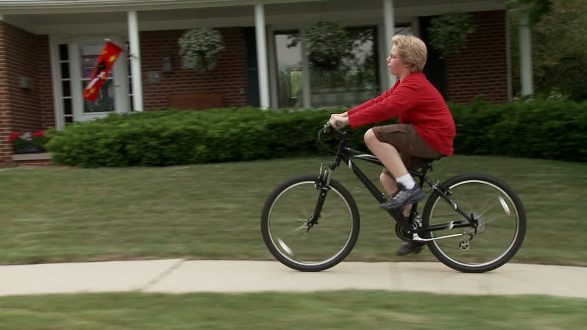Young cyclist rides on sidewalk in middle-class, mid-west American suburb. 