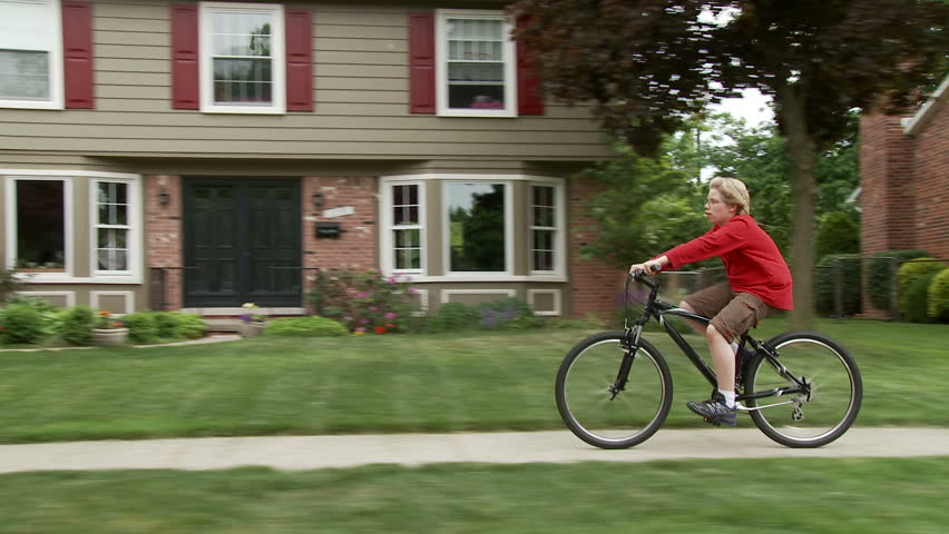 Young cyclist rides bike on sidewalk in a middle-class, mid-western American