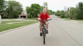 Boy riding a bicycle in the road through middle-class Mid Western American suburb.  Recorded from a moving vehicle with camera mounted on a gyroscopic stabilizer.  Boy exits frame at end of clip.