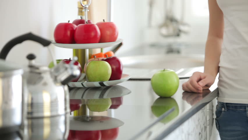Young woman standing in kitchen holding apple and smiling
