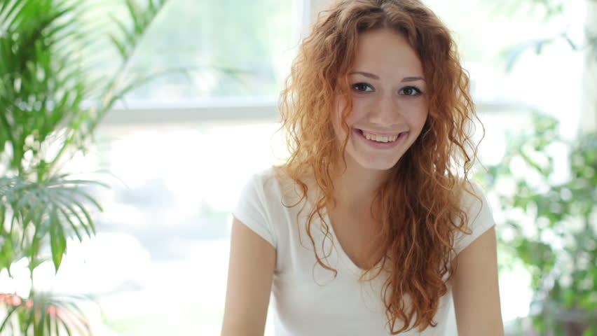 Young woman sitting at table using touchpad and smiling at camera
