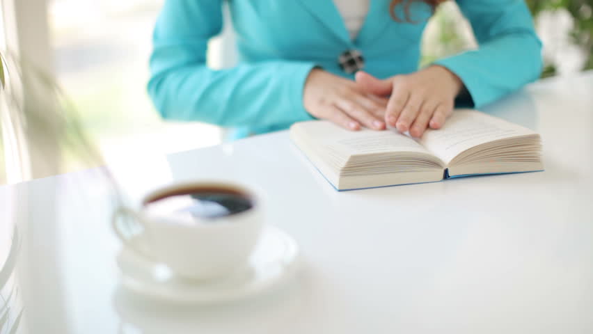 Young woman sitting at table with book and cup of coffee
