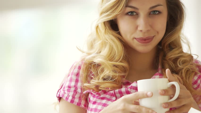 Pretty blond girl holding cup of drink and smiling at camera
