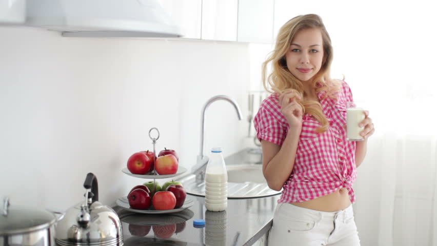 Pretty girl in kitchen holding glass of milk and smiling
