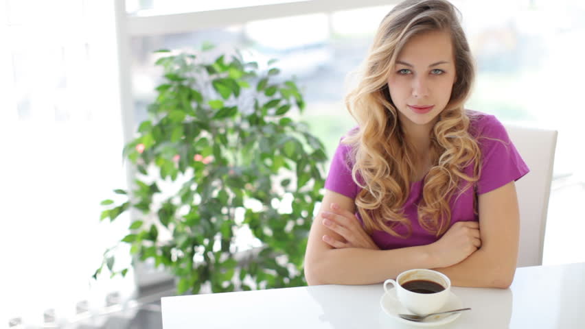 Young woman sitting at table with cup of coffee  and smiling at camera
