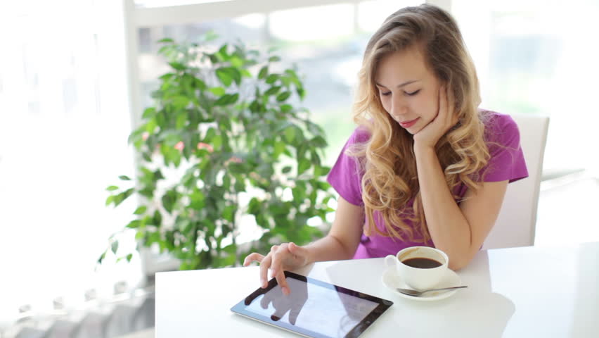 Young woman sitting at table with cup of coffee and using touchpad
