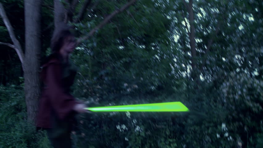 Two men duel with futuristic glowing green laser swords.  Fighting on grassland