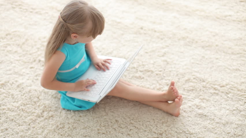 Funny young girl sitting on floor with laptop and gesturing at camera with her