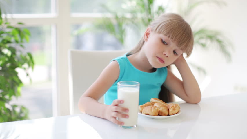 Pretty little girl sitting at kitchen table holding glass of milk in her hand