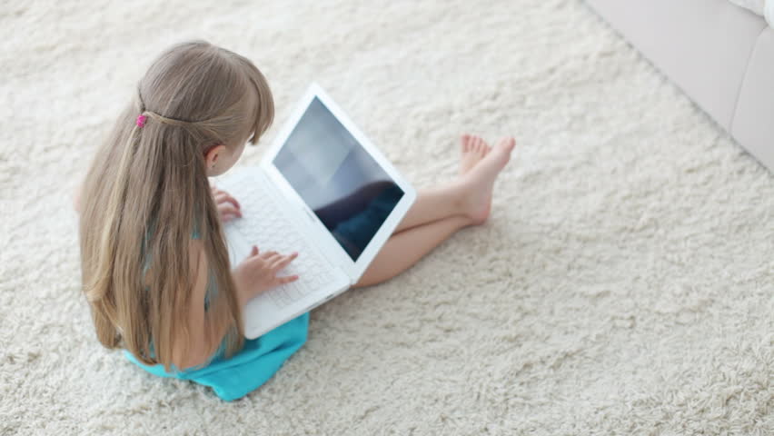 Pretty little girl lying on floor using laptop and smiling at camera
