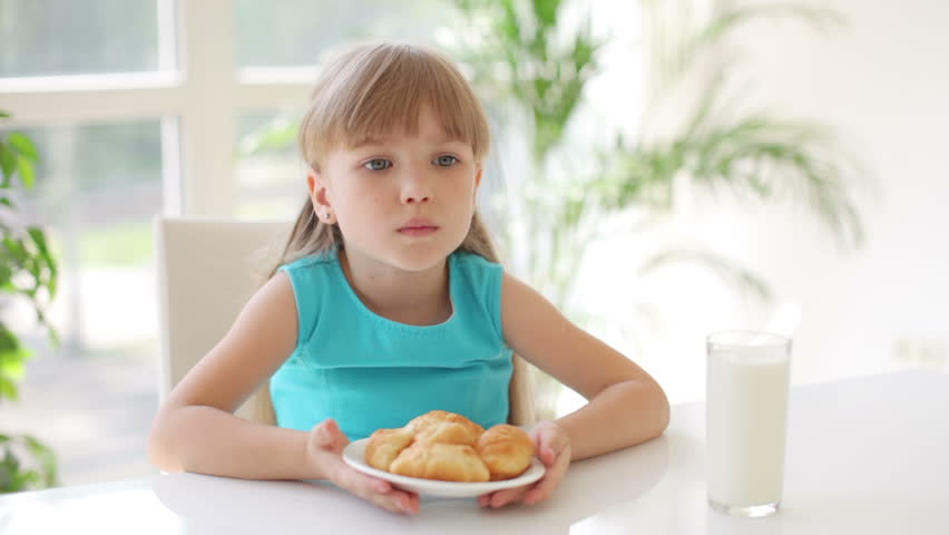 Funny little girl sitting at kitchen table holding plate of cakes in front of