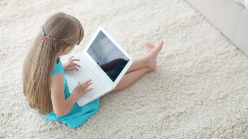 Funny little girl sitting on floor with laptop and smiling at camera

