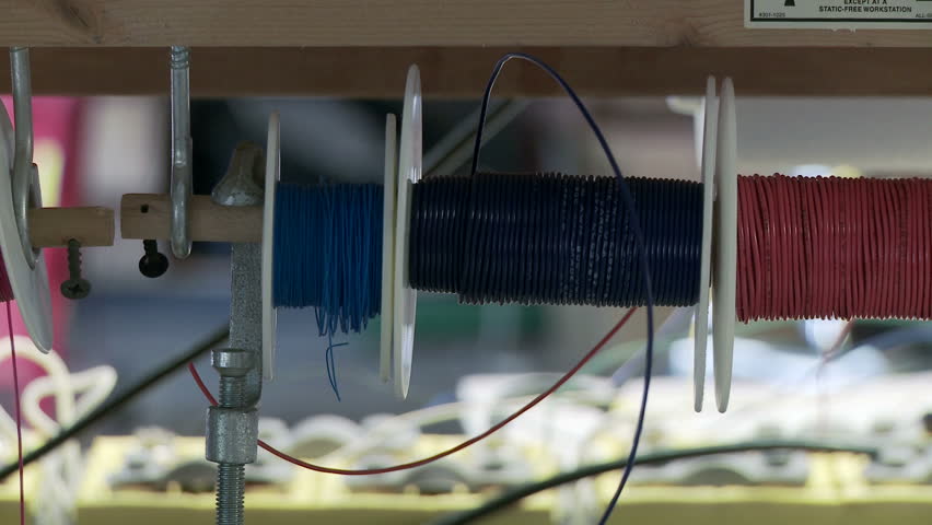 Tracking past reels of different colored electric wire in a workshop.