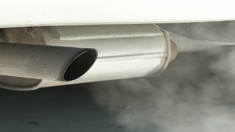 View of car exhaust pipe, emitting fumes, with details of car underside included.  Dolly in from right, at an angle to the car.