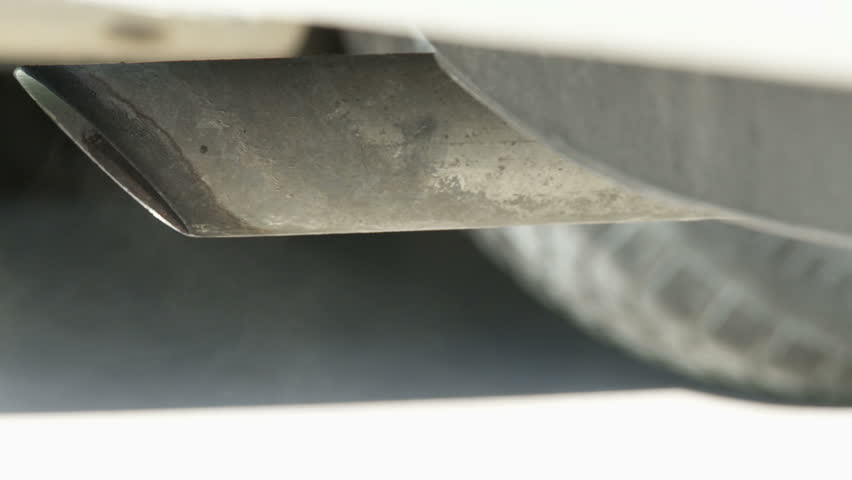 View of car exhaust pipe, emitting fumes, with very shallow depth of field. 