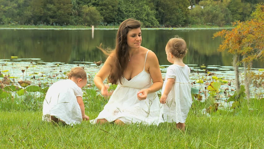 Young Caucasian mom enjoying outing park with cute little blonde twin daughters