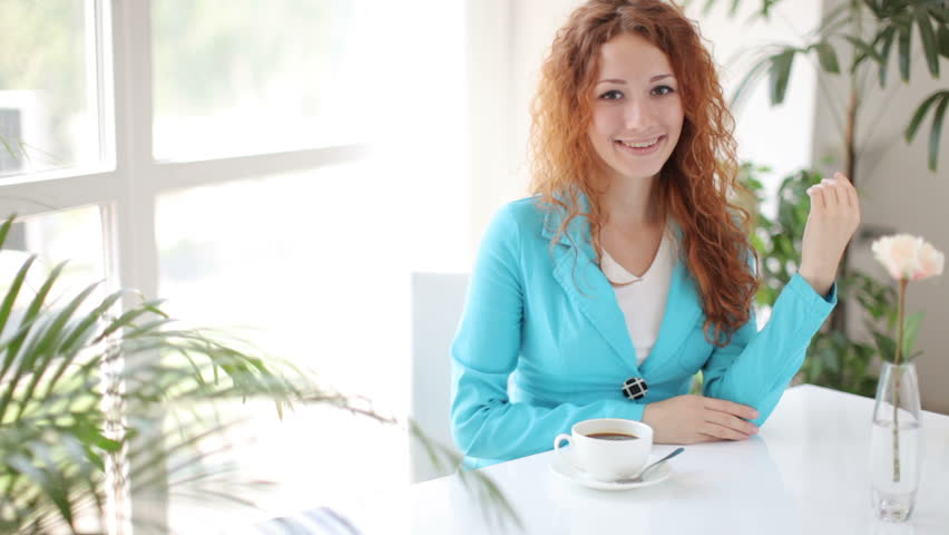 Young woman siting at table holding cup of coffee and smiling

