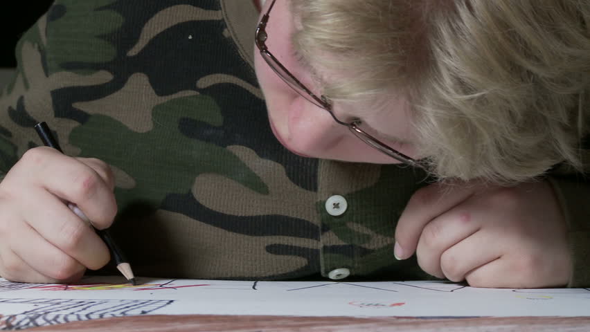 Tracking from right to left, camera reveals close up of a boy drawing.