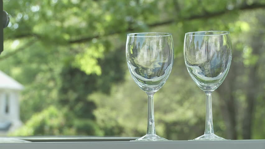 Two glasses of white wine are poured from a bottle.  Outdoor bar.  Dolly shot