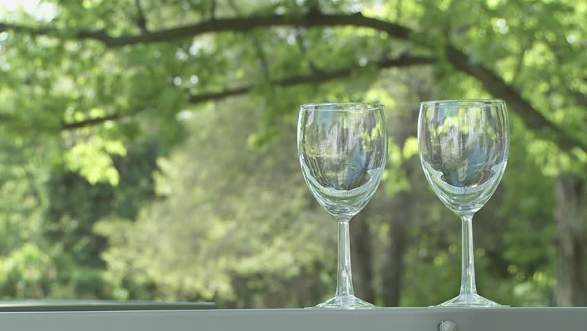 Two glasses of white wine are poured from a bottle.  Outdoor bar.  Dolly shot