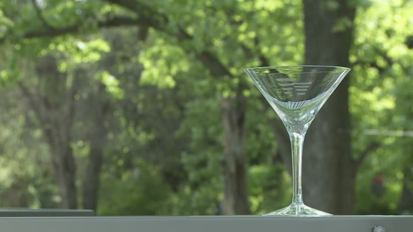 Martini poured into a glass on an outdoor bar.  Centered with trees behind. 
