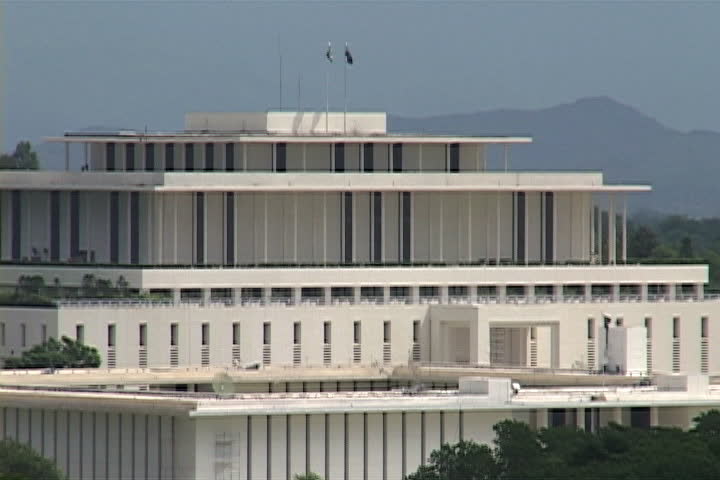 CU Pakistan Secretariat building, camera pulls back to also show the Parliament House and tree line in Islamabad, Pakistan.