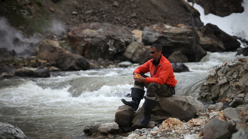 Man sitting on trunk on mountain trail. Mountain stream with stones