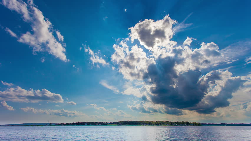Beautiful time lapse of rays of sunlight breaking through big white clouds over the water.