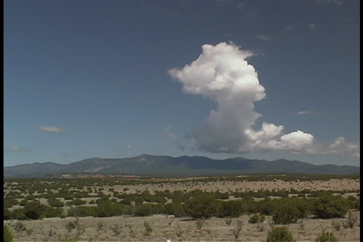 Puffy white cloud in blue sky over flat, open plain in Albuquerque, New Mexico. Salinas Mountains are in background.