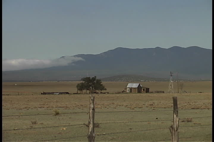 Farm and windmill on a flat, open plain with the Sandia Mountains in background in Albuquerque, New Mexico.