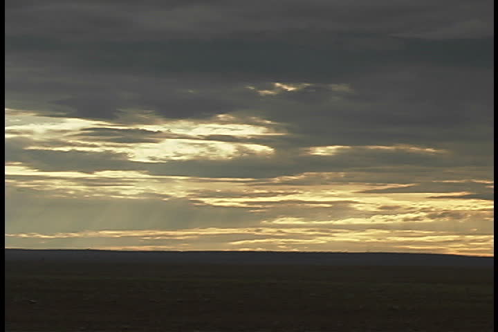 Open plain with flat horizon, sun dappled clouds hang low in sky in Albuquerque, New Mexico.