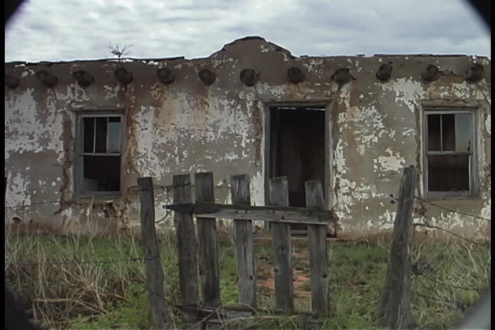 Abandoned adobe house, with broken glass in windows and old broken picket fence in front in Albuquerque, New Mexico.