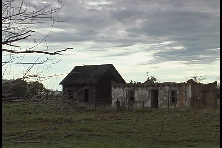 Two abandoned houses on plain with dark, low clouds overhead in Albuquerque, New Mexico.