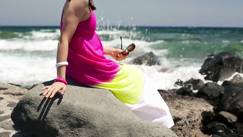 Pensive woman sitting on rocks by the sea
