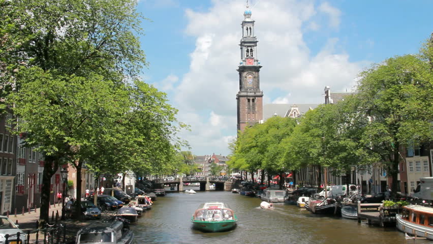 Tour boat sails in Amsterdam canal,with Westerkerk tower in the background in Amsterdam, Holland